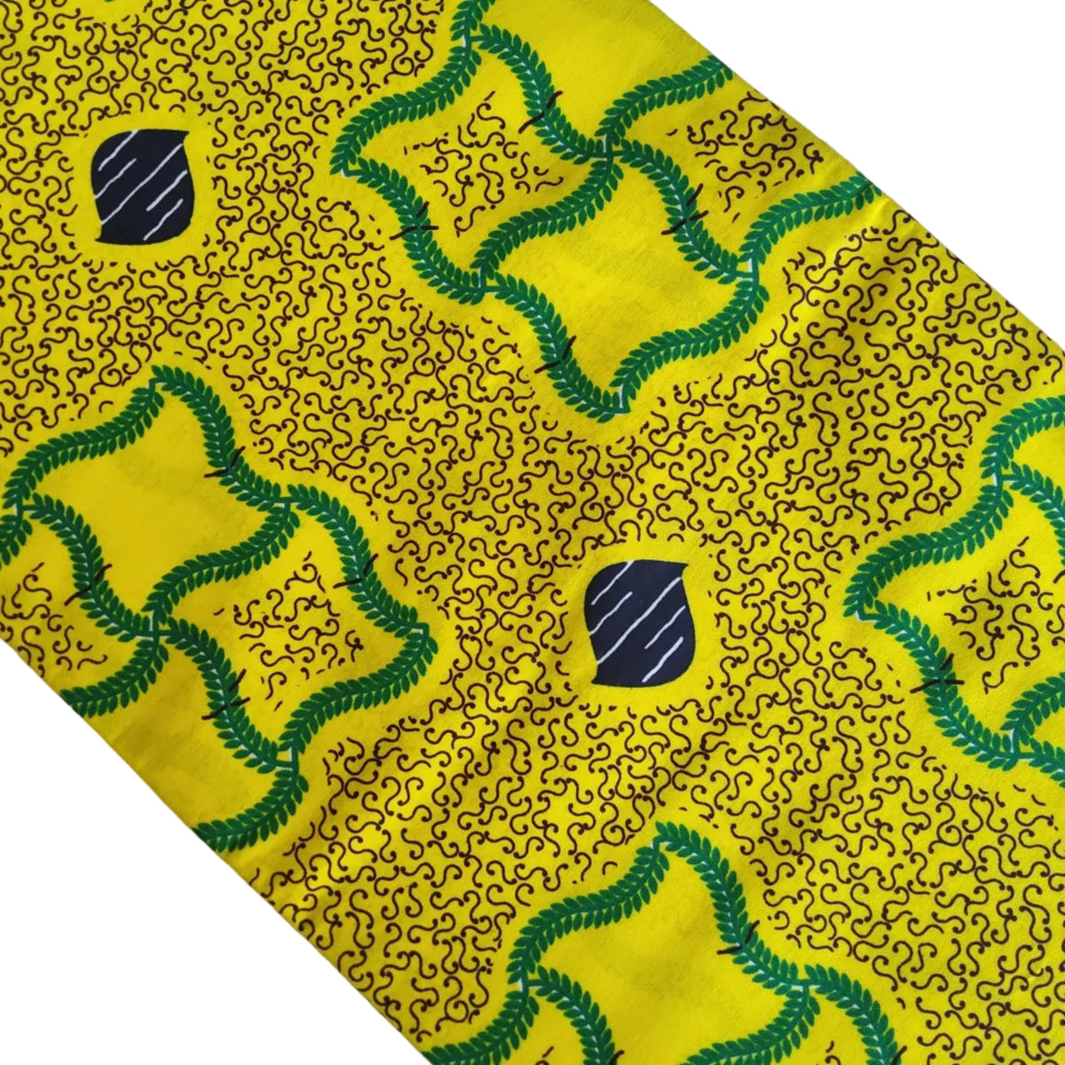 Yellow African wax print fabric with green and black dotted patterns and small navy blue shield motifs, laid diagonally on a white surface.