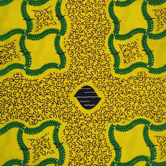 A rectangular piece of yellow African wax print fabric with a green and black geometric pattern, laid flat on a white sheet.