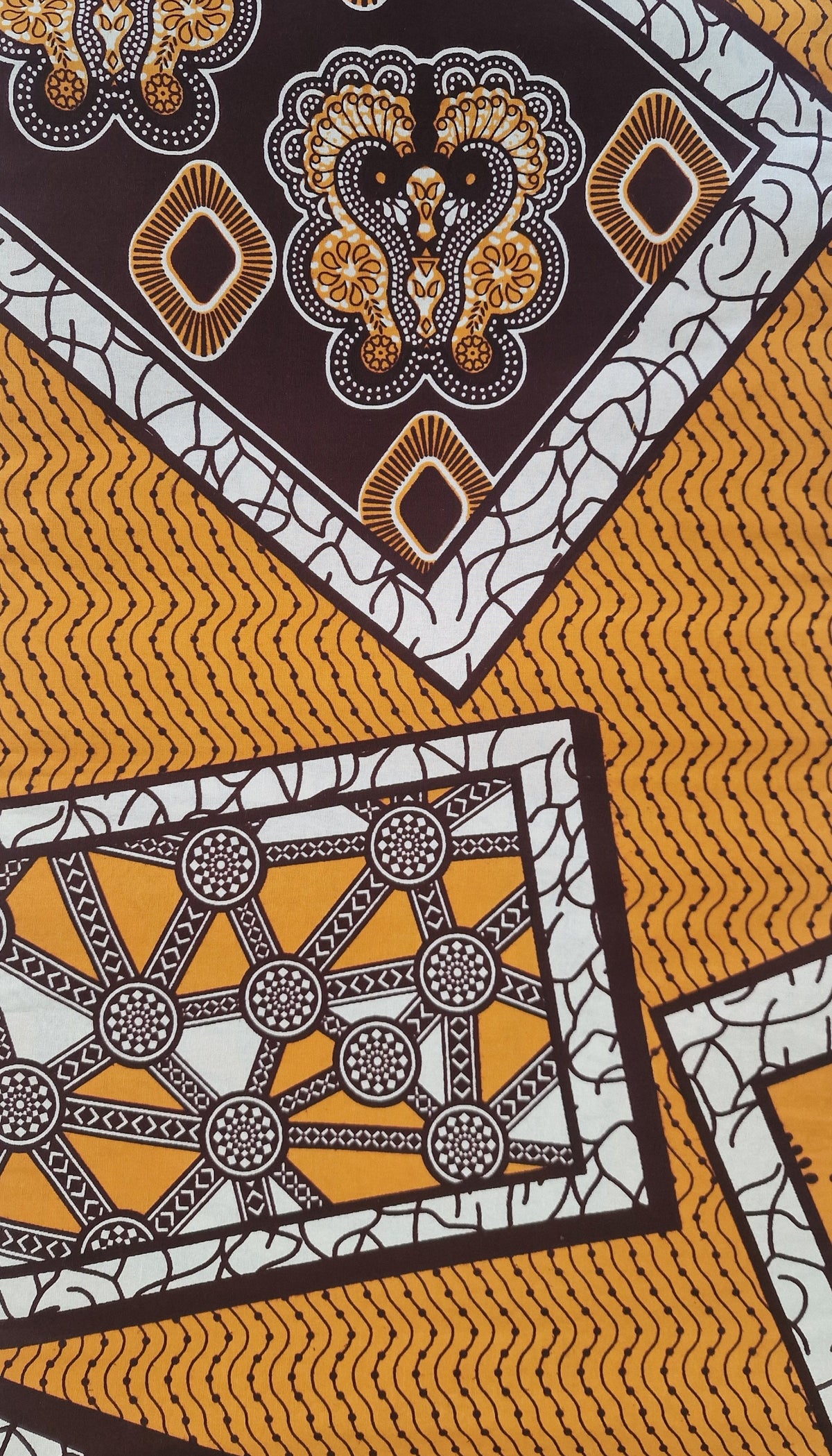 Patterned Ankara print featuring bold geometric and ornamental motifs in mustard yellow, white, dark brown, and black.