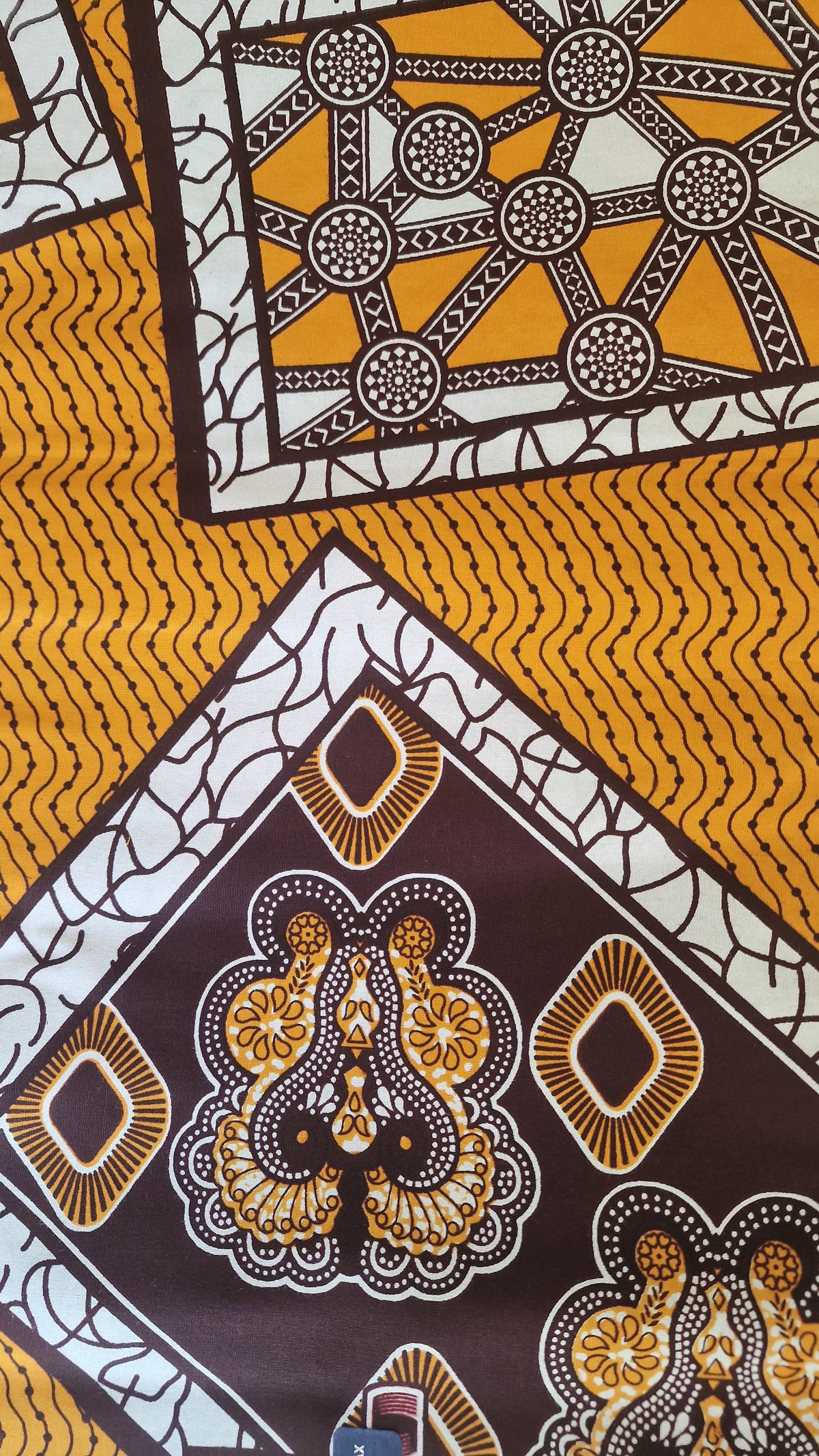 Patterned Ankara print featuring bold geometric and ornamental motifs in mustard yellow, white, dark brown, and black.