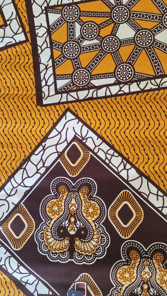 Patterned Ankara print featuring bold geometric and ornamental motifs in mustard yellow, white, dark brown, and black.