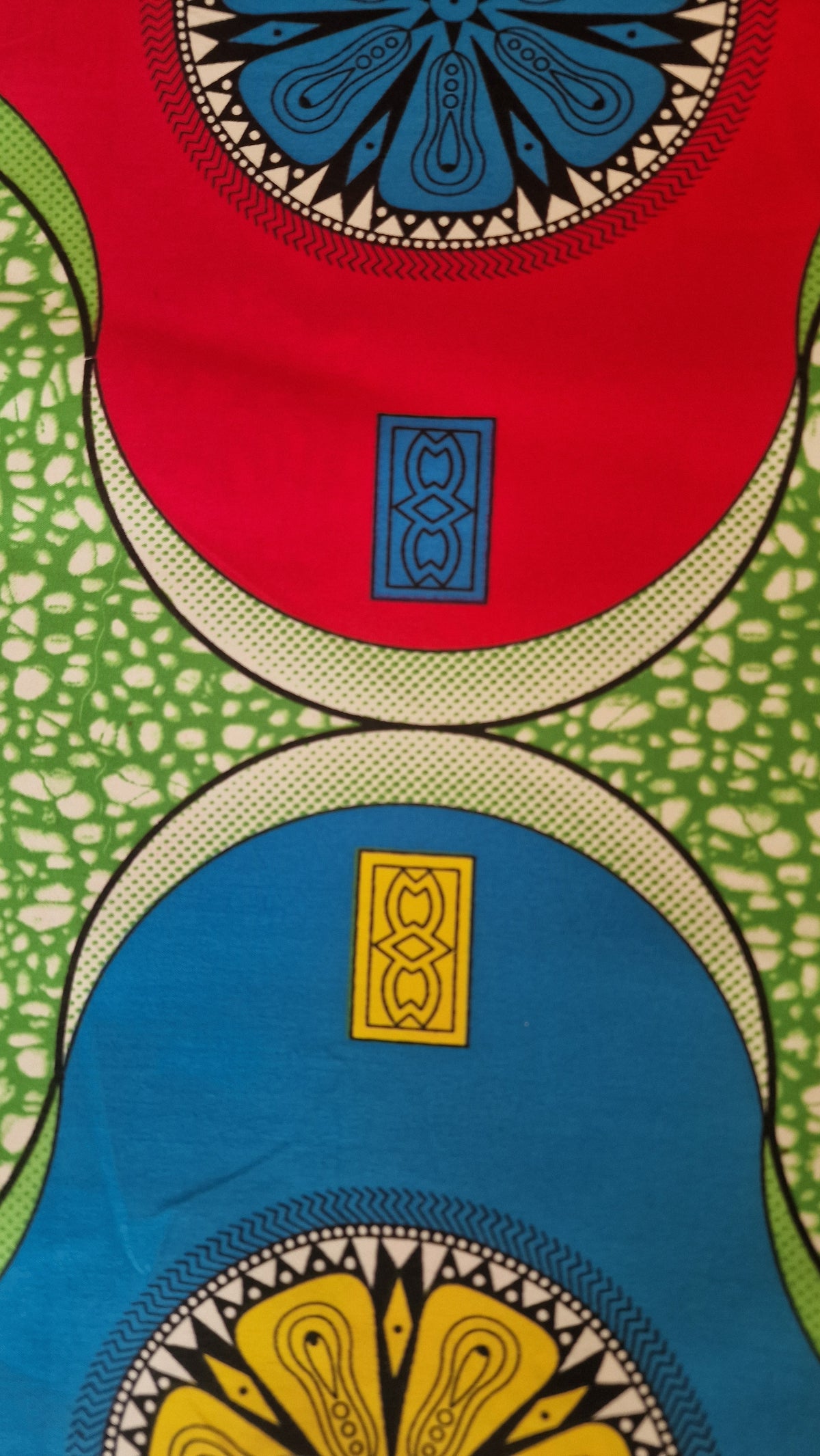 Vibrant African wax print fabric featuring a bold geometric pattern with large red, green, and blue circular shapes and intricate black and yellow details.