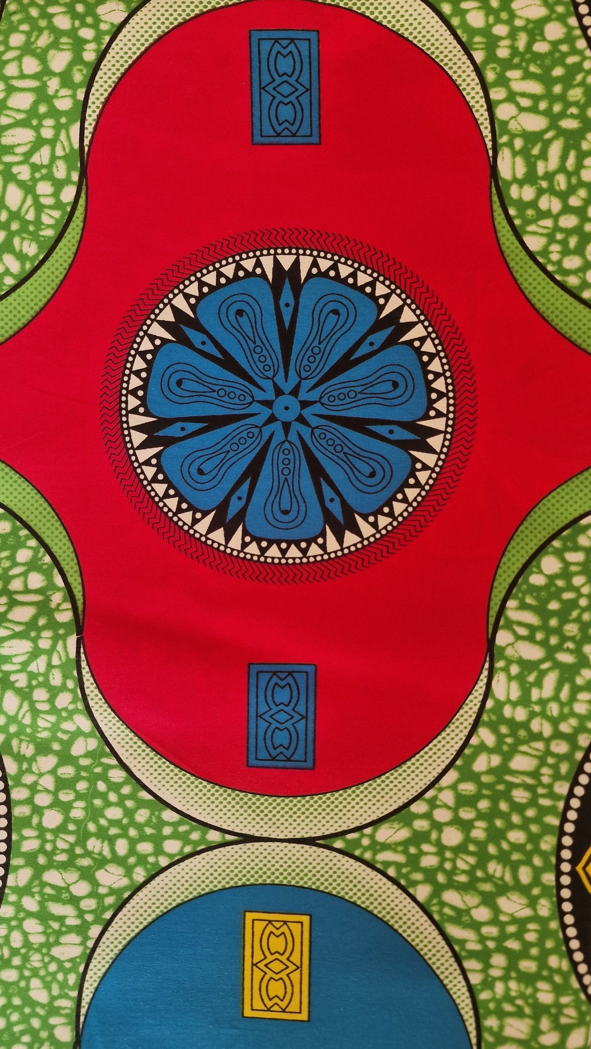 Vibrant African wax print fabric featuring a bold geometric pattern with large red, green, and blue circular shapes and intricate black and yellow details.
