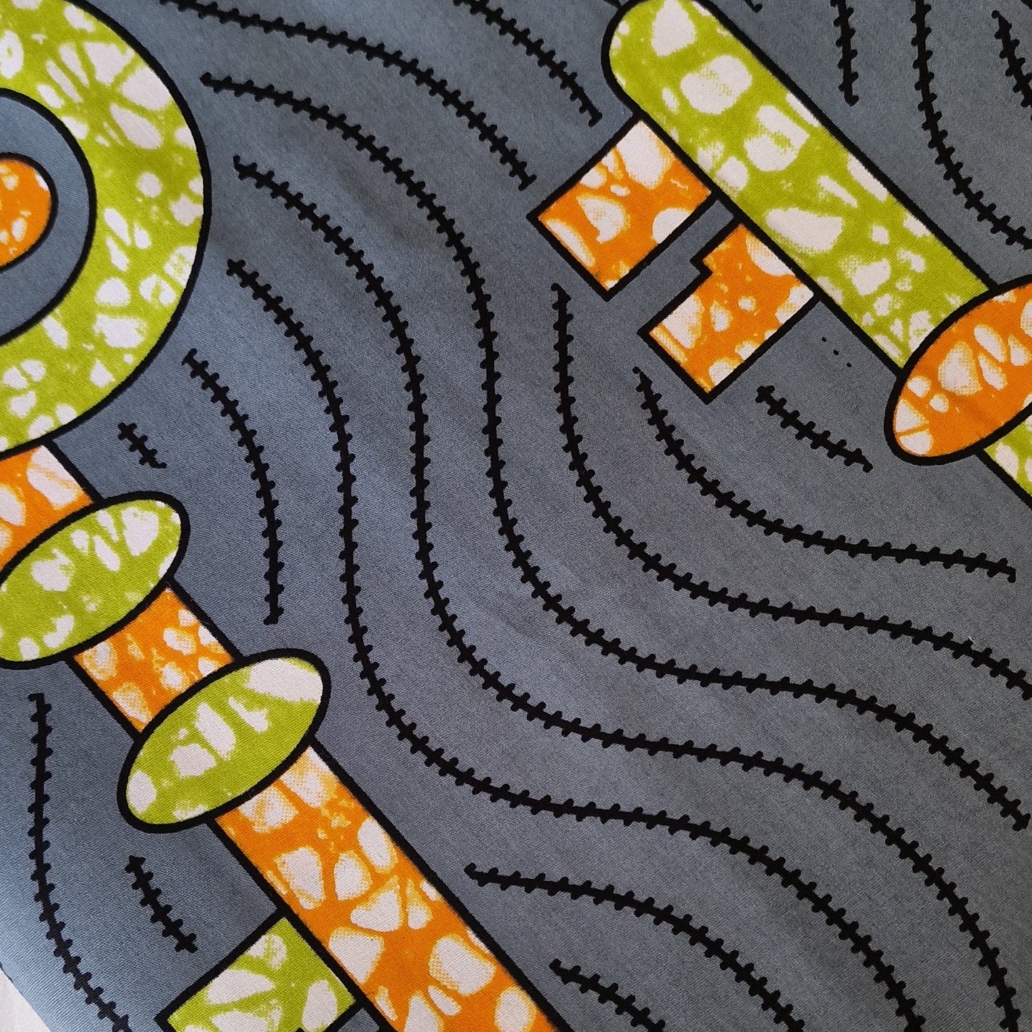 African wax print pattern featuring  orange and green mix key motifs on a gray background.